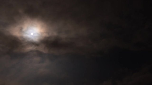 The moon is visible and hiding behind black clouds. Night for vampires. Time-lapse video.