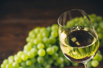 White wine full in wine glasses with a bunch of green grapes, on a wooden background