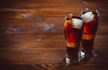 Beautiful cold fizzy cola soda with cubes ice in glasses goblet on old wooden background with free space. Shallow DOF.