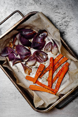Roasted vegetables carrot and red onion on baking tray on rustic metallic background. Top view with copy space.