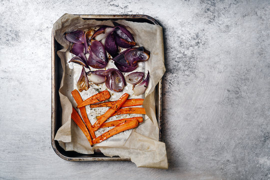 Roasted vegetables carrot and red onion on baking tray on rustic metallic background. Top view with copy space.