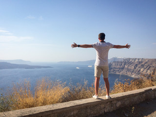 A man looks at the sea with his hands spread wide on a hot summer day