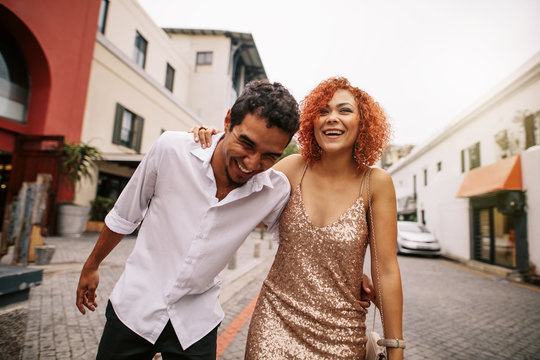 Young man and woman laughing while walking on street.
