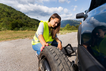 Young girl changing the tire of her broken car in the forest