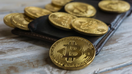 Golden Bitcoins with leather wallet on a wooden table .Close up side view