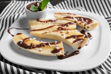 Plate with delicious sliced bananas and chocolate sauce on table