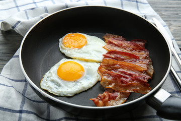 Frying pan with eggs and bacon on table