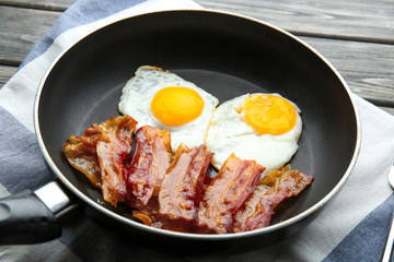 Frying pan with eggs and bacon on table
