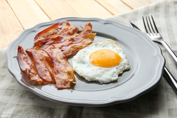 Plate with fried egg and bacon on table