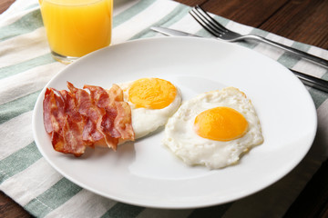 Plate with fried eggs and bacon on table