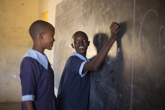 School girls writing on chalkboard in classroom. Kenya, Africa.