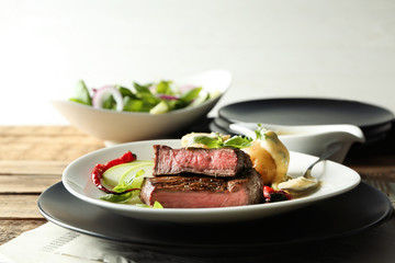 Plates with delicious sliced meat, sauce and vegetables on wooden table