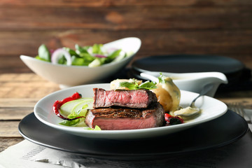 Plates with delicious sliced meat, sauce and vegetables on wooden table