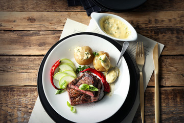Plate with delicious sliced meat, sauce and vegetables on wooden table