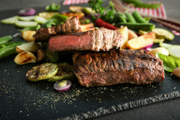 Delicious sliced meat, sauce and vegetables on slate plate