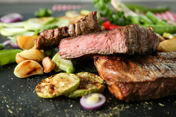 Delicious sliced meat, sauce and vegetables on slate plate