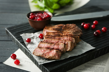 Cutting board with delicious sliced meat and cranberry sauce on wooden table