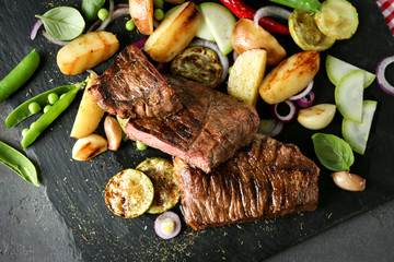 Delicious sliced meat, sauce and vegetables on slate plate