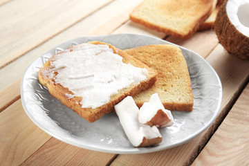 Delicious toasts with coconut oil in plate on wooden table