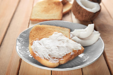 Delicious toasts with coconut oil in plate on wooden table