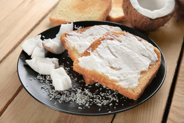 Delicious toasts with coconut oil in plate on wooden table