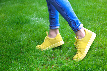 Female legs in jeans and yellow sneakers on green grass