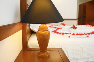 Night stand with lamp and big bed decorated with flowers in hotel room