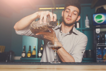 Young bartender pouring cocktail drink into glass