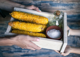 Female and children's hands hold a box with boiled tasty corn. Easy toning. Selective focus