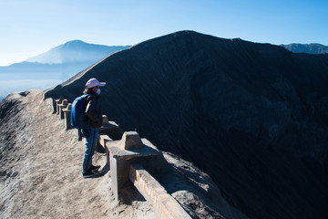 Woman tourism standing on top of crater view point at Mount Bromo volcano, view behind is Mount Batok JAVA, INDONESIA.
