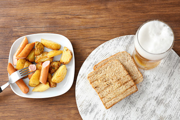 Plate with potato and sausages near glass of bear on table