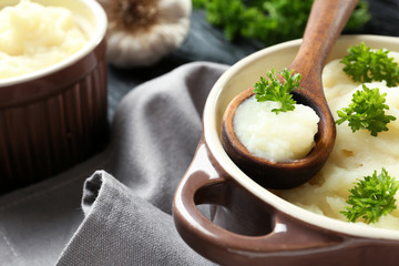 Casserole and wooden spoon with mashed potatoes on table, closeup