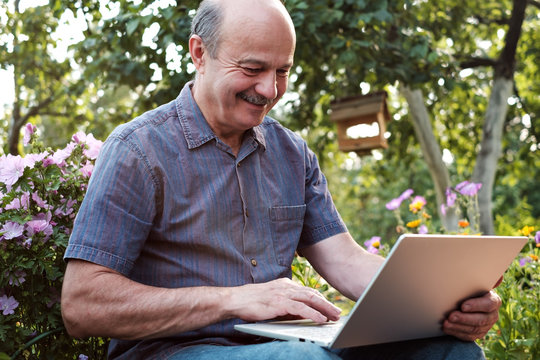 Mature man sitting in garden in countryside with notebook and relaxing