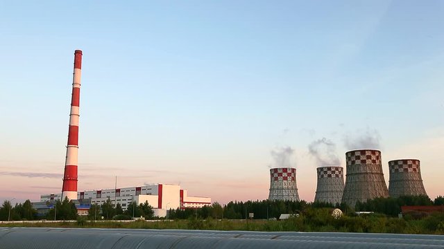 Thermal Power Station edge of city summer evening dolly shot. Smoke go up to blue sky. Energy production and pollution. This is a modern urban landscape. Chimney-stalk and ecology problem on Earth.
