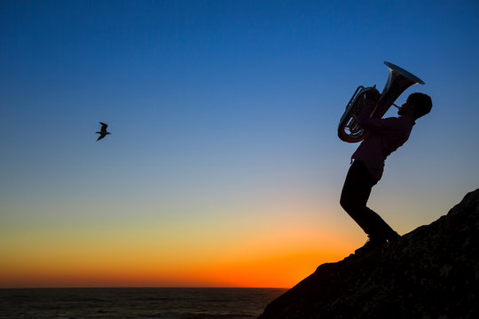 Silhouette of musician play Tuba on sea shore at amazing sunset.