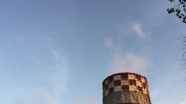 Cogeneration power plant in city. Tilting down from blue sky to pipes tubes chimney-stalk. Thermal Power Station chimney smoke sky. Sunset landscape. Combined heat and power plant near megapolis.