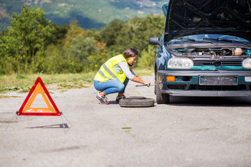 Female changing the tire of her car at the highway