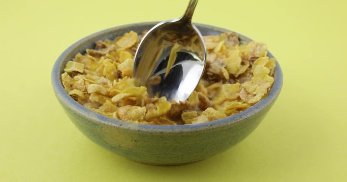 A full bowl with multigrain breakfast cereal with skim milk being stirred then one bite taken.