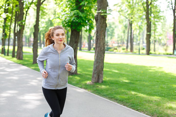 Young woman jogging in green park, copy space