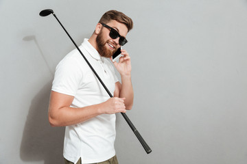 Side view of Calm golfer in sunglasses talking by smartphone