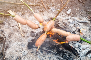 Sausages on sticks are fried on a fire, sunny