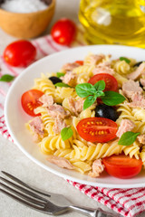 Fusilli pasta salad with tuna, tomatoes, black olives and basil on gray stone background