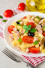 Fusilli pasta salad with tuna, tomatoes, black olives and basil on gray stone background