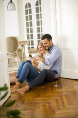 Young couple sits on the floor, drinking red wine and woman using cell phone