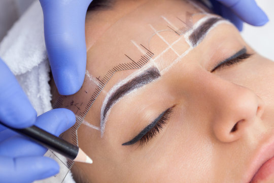 Fototapeta Permanent make-up for eyebrows of beautiful woman with thick brows in beauty salon. Closeup beautician doing  tattooing eyebrow.