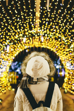 Back view of woman with backpack standing under illuminated garl