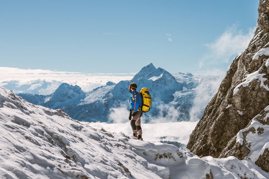 male mountaineer with yellow backpack overlooking snowcovered mo