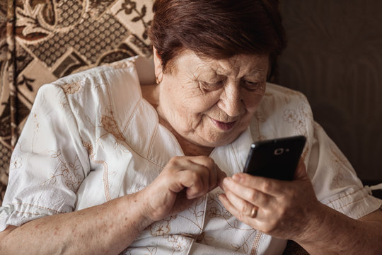 Old woman using smartphone (tablet) sitting in chair smiling