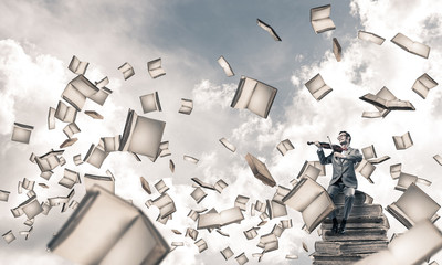 Handsome violinist sitting on book and play his melody