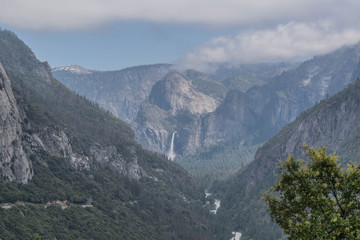 View of Yosemite Valley, Bridalveil waterfall, Merced river and surrounding mountains, with cloudy blue sky, in Yosemite National Park